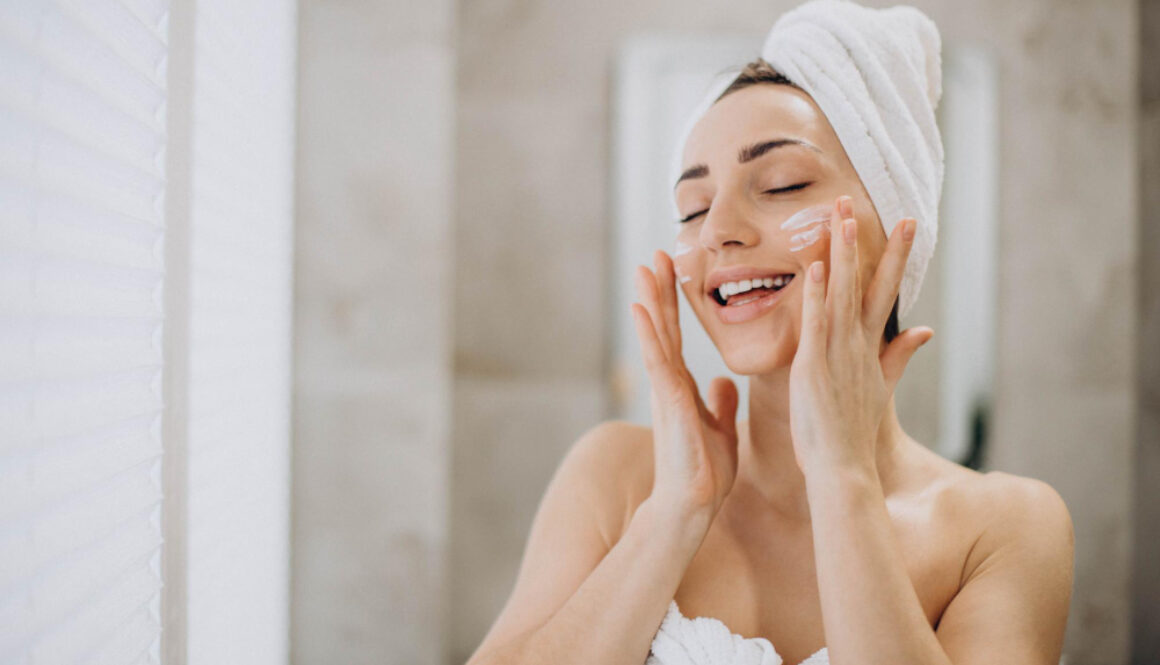 young-woman-applying-face-cream-her-face-with-towel-head