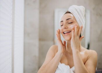 young-woman-applying-face-cream-her-face-with-towel-head