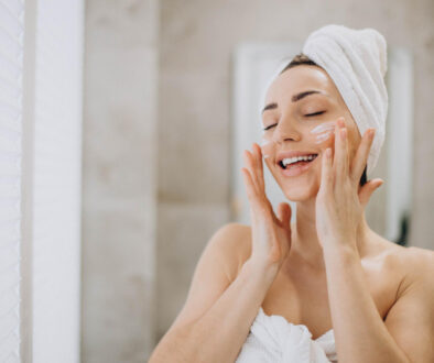 young-woman-applying-face-cream-her-face-with-towel-head