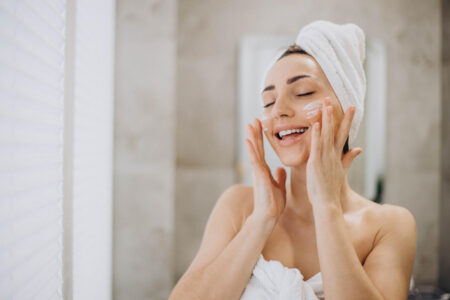 young-woman-applying-face-cream-her-face-with-towel-head